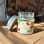 Bougie artisanale Fraise des bois Les Lueurs d’Horion ouverte, montrant la cire blanche dans un pot en verre sur une surface en bois.
