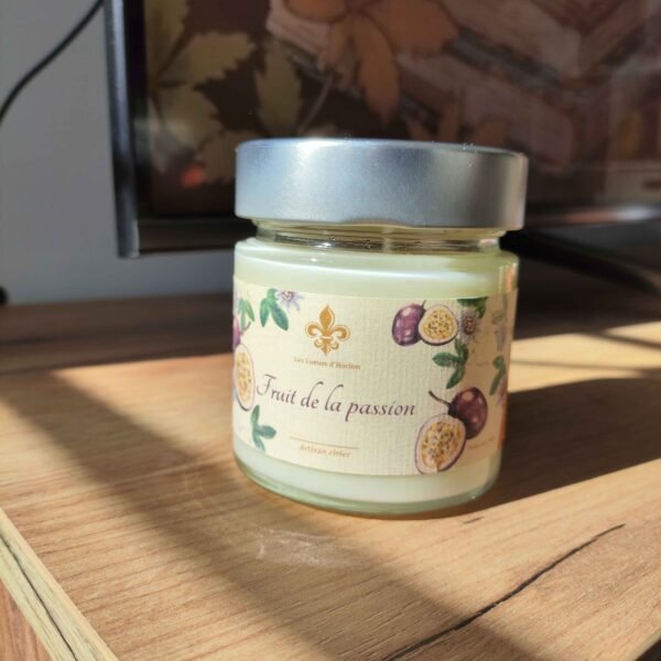 Bougie artisanale Fruit de la passion Les Lueurs d’Horion en verre avec couvercle en métal, posée sur une surface en bois, éclairée par le soleil.