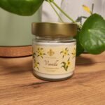 Bougie à la Vanille Les Lueurs d'Horion sur bois, avec plante verte et terrarium en arrière-plan.